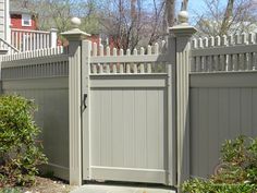 a gray fence with a gate and some bushes