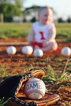 a baby sitting on the ground next to baseballs and mitts with an infant in the background