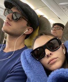 two people sitting on an airplane with headphones in their ears and one person wearing sunglasses