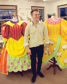 a man standing next to two dresses on mannequins