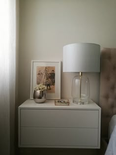 a nightstand with a lamp and pictures on it