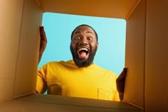 a man in a yellow shirt is opening a box with his mouth wide open and looking up