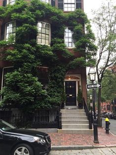 a black car parked in front of a tall building with ivy growing on it's side