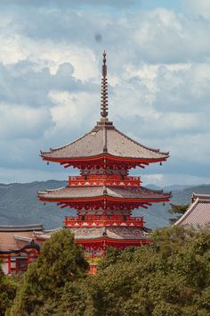 a tall red and white pagoda with trees in the foreground on a cloudy day