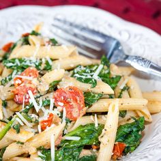 pasta with spinach, tomatoes and parmesan cheese on a white plate next to a fork