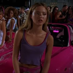 the girl next door is standing in front of her pink car and other girls are looking on