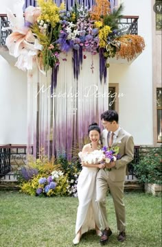 a man and woman standing next to each other in front of a building with flowers on it