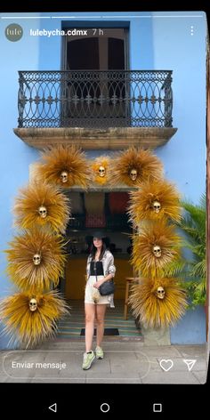 a woman standing in front of a blue building with yellow flowers on the door and balcony