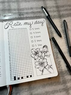 an open notebook with some flowers on it next to pens and pencils in front of it