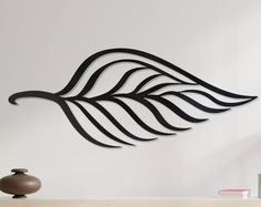 a metal wall sculpture with black lines on it's side and a vase next to it