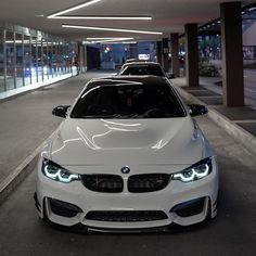 two white cars parked next to each other in an empty parking garage with lights on