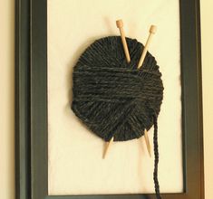 there is a yarn ball and two knitting needles on the wall next to a frame