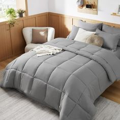 a bed with grey comforter and pillows in a room