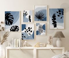 a white table topped with books and vases filled with plants next to pictures on the wall