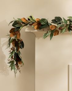 a wreath with leaves and berries hanging from the wall next to a white fireplace mantel