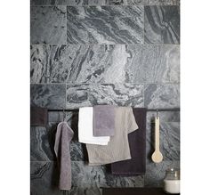 towels are hanging on a rack in front of a marble tile wall with gray and white colors