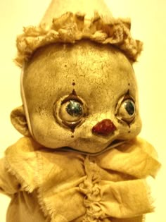 an old teddy bear wearing a yellow dress and hat with eyes wide open, sitting on a white surface