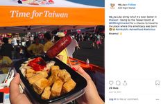 someone is holding up a plate of food at an outdoor event with people in the background