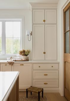 a kitchen with white cupboards and wooden flooring next to a window in the wall