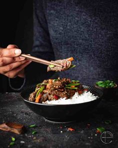 someone is holding chopsticks over a bowl of rice and beef stir fry with vegetables