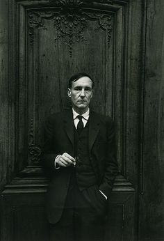 a black and white photo of a man in a suit leaning against a wooden door