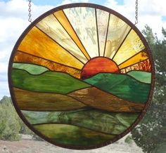 a stained glass sun catcher hanging from a chain in front of a tree and sky