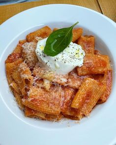 a white plate topped with pasta covered in sauce and cheese next to a green leaf