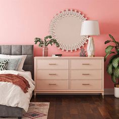 a bedroom with pink walls and wooden flooring, a large round mirror above the bed