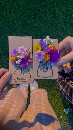 two people holding flowers in front of each other on the grass with one person's hand