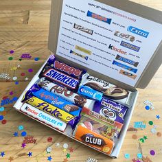 an open box filled with assorted candy on top of a wooden floor covered in confetti