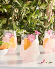 three glasses filled with different types of drinks on a white table next to green plants