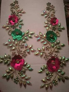 two pink and green flower brooches are on a white tablecloth with silver sequins