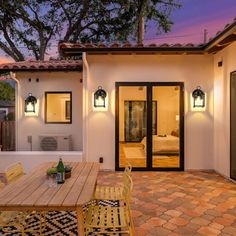 a patio with table, chairs and lights on it at dusk or dawn in front of a house