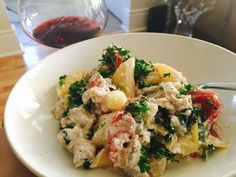 a white plate topped with pasta and veggies next to a glass of wine