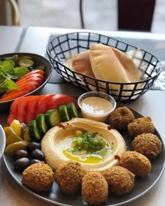 an assortment of food on a plate with dipping sauces and vegetables in the background