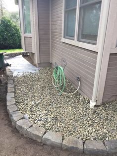 a hose is attached to the side of a house with rocks in front of it