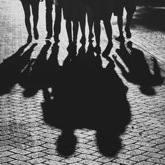 a group of people walking down a street with their shadows on the ground behind them