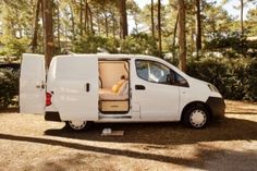 a small white van is parked in the woods with its door open and it's seat up