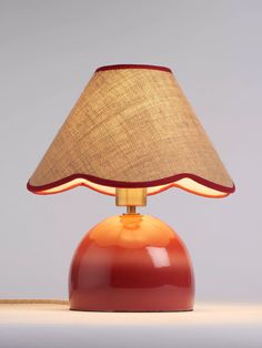 an orange lamp with a brown shade on the top and red base, sitting on a white surface