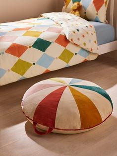 a small child's bedroom with a colorful bed and round floor pillow on the floor