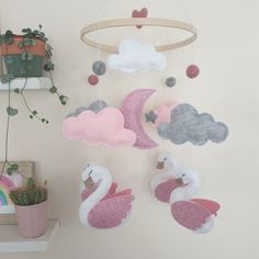 a pink and white mobile hanging from a wall next to a potted plant