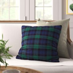 a green and blue plaid pillow sitting on top of a white couch next to a potted plant