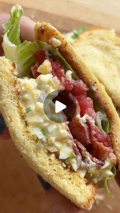 a hand holding a sandwich with lettuce, tomatoes and other toppings on it