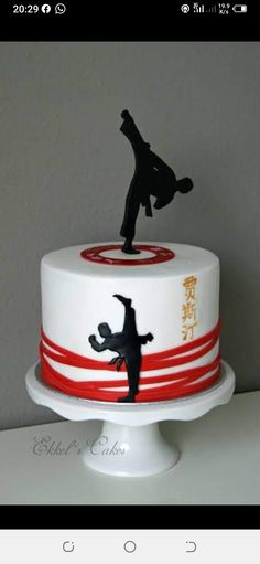 a white cake with a red and black design on the top has a silhouette of a man doing a kickflip