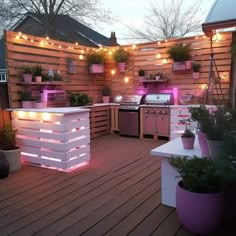 an outdoor kitchen with potted plants and lights on the outside wall, next to a deck