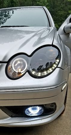 the front end of a silver car with its lights on