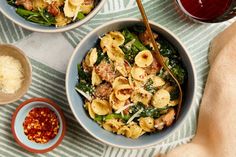 three bowls filled with pasta and vegetables on top of a striped table cloth next to two glasses of wine