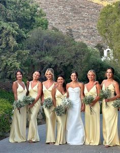 a group of women standing next to each other in front of some trees and bushes