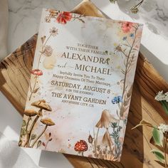 a wedding card on top of a wooden tray next to flowers and greenery in the background