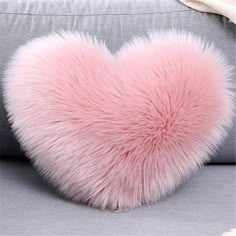 a pink heart shaped pillow sitting on top of a gray couch next to a white blanket